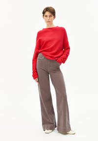 Rode geribbelde trui met een losse pasvorm, gecombineerd met wijde taupe corduroy broeken. De broeken hebben voorzakken en een afgewerkte rand.
