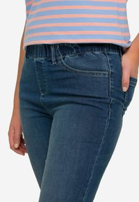 Vaqueros de mezclilla en azul oscuro con una cintura elástica, que cuentan con un bolsillo frontal, textura suave y una silueta ajustada.