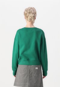 Felpa verde in cotone con scollo a girocollo, spalle scese e bordo a costine. Abbinata a una gonna a righe bianche e nere.