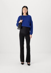 Blå oversized genser, sorte høytlivsbukser og svarte hælersko. Enkel design med en avslappet passform og glatt tekstur. Svart håndveske.