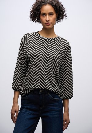 Zwart-witte blouse met chevronpatroon, driekwartmouwen, ontspannen pasvorm, zachte textuur, gecombineerd met donkerblauwe jeans.