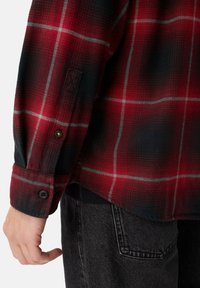 Rød og sort ternet flannel skjorte med knapmansjetter, prydet med et struktureret stof og gråt rutenet mønster. Kombineret med mørke jeans.