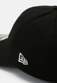 Căciulă de baseball neagră cu un material texturat, visieră curbată și un logo brodat alb pe lateral. Vizibile șase guri de ventilație.