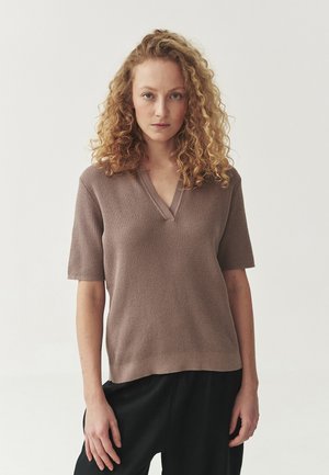 Maglione a maniche corte con scollatura a V in un morbido tessuto a maglia color marrone chiaro. L'orlo è dritto. Abbinato a pantaloni neri larghi. Design minimalista.