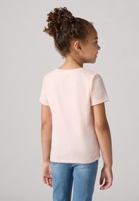 Camiseta de algodón de color rosa claro con mangas cortas, escote redondo y una textura suave, combinada con jeans de mezclilla azul.