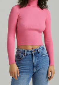 Fitted pink ribbed turtleneck top with long sleeves, paired with high-waisted light blue denim jeans featuring a single button closure.