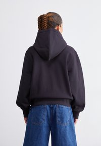 Sweatshirt à capuche noire avec une coupe décontractée et des poignets côtelés, associé à un jean en denim large de couleur bleu clair, vu de dos.