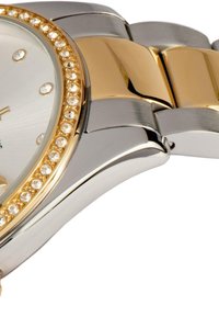 Guld- och silvertonad armbandsur med en rund urtavla, kristallaccenter runt boetten och ett metallänkarmband. Slät polerad yta.