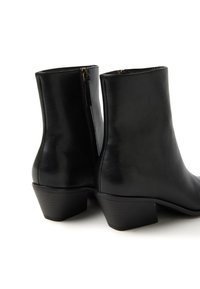 Botas de cuero negras hasta el tobillo con una textura suave, que cuentan con un tacón bajo apilado y un cierre lateral con cremallera.