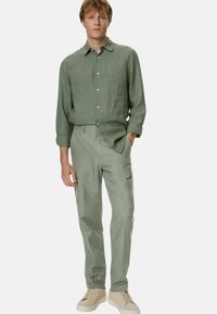 Lichtgroen linnen overhemd met knopen in combinatie met lichtgroene broek en beige sneakers. De outfit heeft een casual, ontspannen pasvorm.