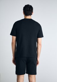 Tricou negru cu manșete scurte, cu o croială dreaptă, asortat cu șorturi negre. Material moale, texturat, cu o croială lejeră.