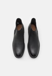 Zapatos de piel negra tipo slip-on con una textura lisa, puntera en forma de almendra y costuras mínimas. Cuentan con plantillas ligeramente acolchadas para mayor comodidad.
