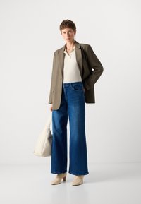 B�éžový blazer, bílý žebrovaný top, široké modré džíny. Modelka drží krémovou kabelku. Hnědé boty na podpatku, minimalistický design, hladké textury.