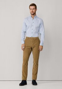 Camisa de botón azul claro con cuello, combinada con pantalones ajustados color caqui y zapatos oscuros; tejido suave, diseño ordenado y aspecto a medida.
