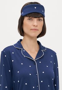 Ναυτικό πιτζάμες με λευκό σχέδιο καρδιάς, διαθέτει γιακά και κουμπιά μπροστά. Ένα ταιριαστό κορδόνι τονίζει την εμφάνιση. Μαλακή, λείη υφή.