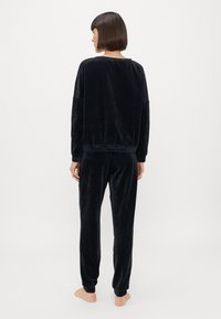 Σέτ loungewear από μαύρο βελουτέ ύφασμα, που περιλαμβάνει μπλούζα με μακριά μανίκια σε χαλαρή γραμμή και tapered παντελόνι με  ribbed μανσέτες και απαλό άγγιγμα.