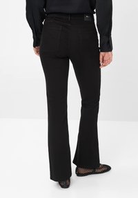 Mustat leveälahkeiset farkut, joissa on takataskut ja vyötäröllä oleva etiketti. Kangas näyttää sileältä, ja malli istuu hyvin lantion kohdalla.