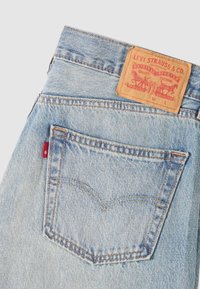 Poche arrière d’un jean en denim bleu clair avec écusson en cuir Levi Strauss et étiquette en tissu rouge.