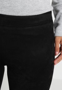 Leggings en suede noir avec une texture lisse, une taille haute et des détails de couture subtils pour un look ajusté.