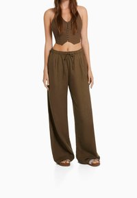 Haut halter cropped marron avec fermeture à boutons et pantalon ample taille haute dans une teinte assortie. Texture douce et coupe décontractée.