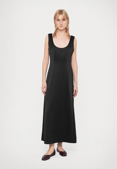 Robe maxi noire sans manches avec un décolleté rond, conçue pour être fluide, en tissu doux. Associée à des ballerines bordeaux.