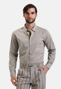 Camicia grigia chiaro con maniche lunghe, texture liscia e colletto normale. Abbinata a pantaloni a righe beige e bianchi.