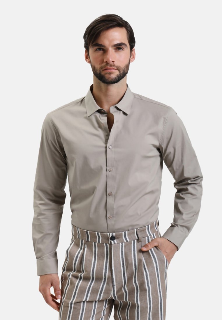 Camicia grigia chiaro con maniche lunghe, texture liscia e colletto normale. Abbinata a pantaloni a righe beige e bianchi.