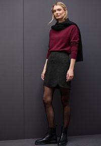 Bordeaux sweater en donkergrijze skaterrock met gegolfde zoom, gecombineerd met zwarte enkelboots en ondoorzichtige tights, tegen een grijze achtergrond.