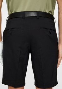 Czarne szorty golfowe z płaskim przodem i podwójnymi tylnymi kieszeniami, z detalami w talii oraz teksturowanym paskiem. Wykonane z gładkiego, lekkiego materiału.