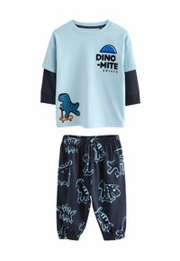 Svijetloplava majica s crnim rukavima sadrži grafiku dinosaura i natpis. Crne hlače s plavim uzorcima dinosaura i elastičnom gumicom.