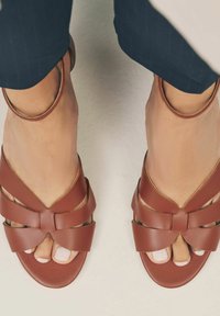 Sandalias de cuero marrón con un diseño en forma de V, que cuentan con varias correas y cortes. Textura suave y estilo de punta abierta.