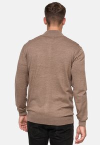Jasno brązowy sweter włóczkowy z długimi rękawami i prążkowanym wykończeniem. Gładka tekstura, minimalistyczny design i okrągły dekolt widoczny z tyłu.