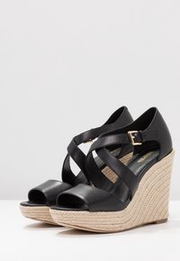 Sandali con zeppa nera in pelle, design con fasce incrociate, punta aperta e zeppa avvolta in juta con un accento di fibbia dorata.