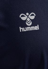 Hvid stiliseret humlebi-logo og "hummel" tekst trykt på mørkeblå tekstureret stof.