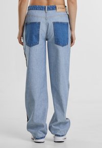 Light blue wide-leg jeans with dark blue back pockets and a branded leather patch on the waistband. Smooth denim texture with a relaxed fit.