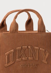Pruun ribatud kangast kott DKNY New York logoga, mis on tikitud ettepoole. Kotil on kaks tugevat käepideme ja hõbedane tõmblukk.