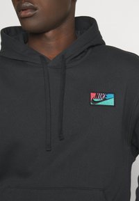 Svart hoodie med dragsnodd, med en flerfärgad broderad Nike-logga på bröstet. Av bomullsmaterial med texturerad finish.