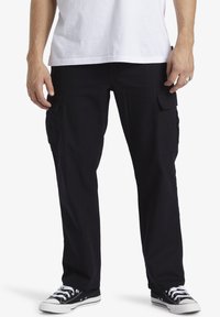 Black cargo pants made of cotton, featuring side pockets, a straight-leg design, and worn with black sneakers and a white T-shirt.