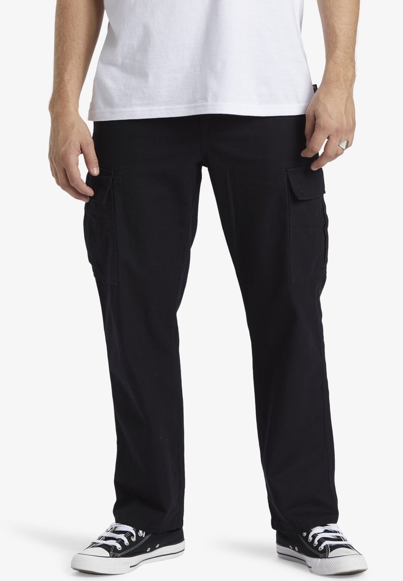 Black cargo pants made of cotton, featuring side pockets, a straight-leg design, and worn with black sneakers and a white T-shirt.