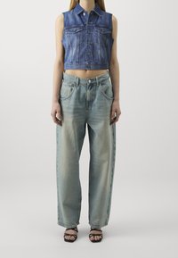 Denim cropped vest with button front and chest pockets, paired with loose-fitting, faded blue high-waisted jeans and black strappy sandals.