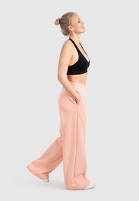 Sujetador deportivo negro con un profundo escote en V, combinado con pantalones de chándal de pierna ancha en un suave color rosa claro, que cuentan con bolsillos laterales y una textura suave.