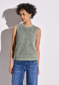 Haut sans manches en tricot vert clair avec motif texturé. Présente un col et un ourlet côtelés. Associé à un jean bleu, mettant en valeur un look décontracté.