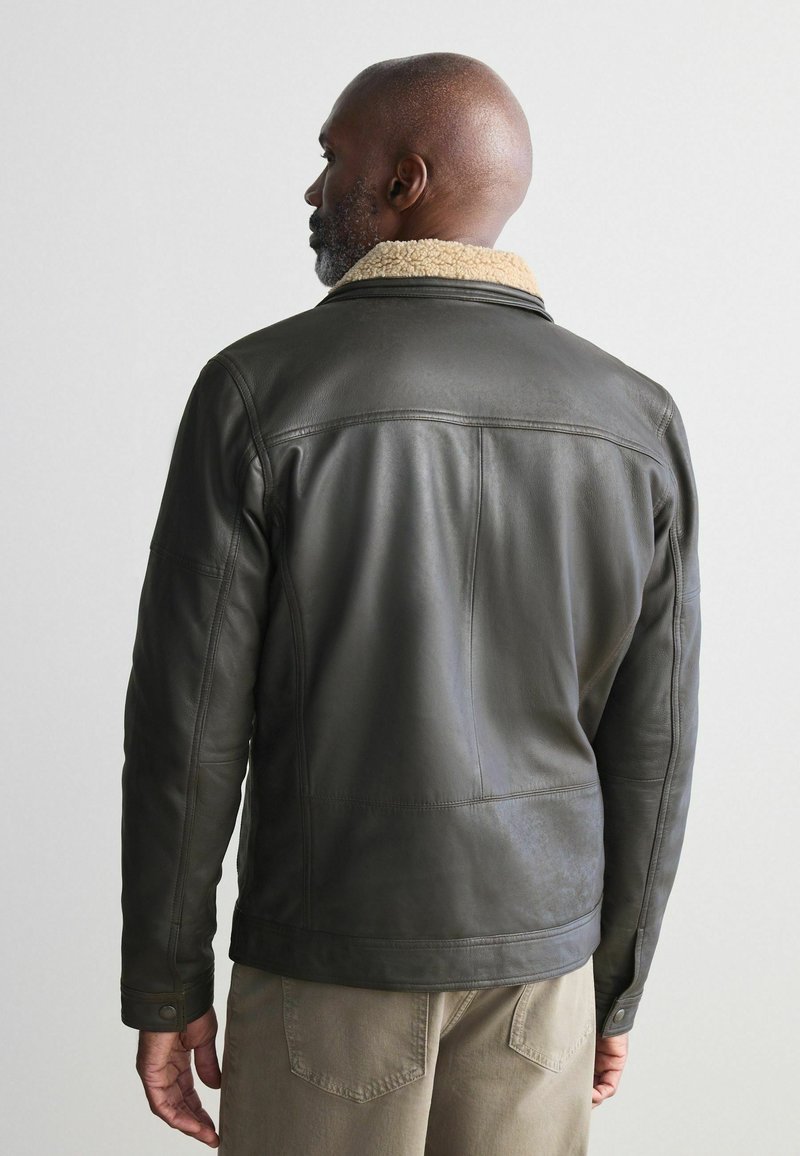 Chaqueta de cuero oscura con un cuello de sherpa beige, forma ajustada y detalles de costura visibles. No se muestra vista frontal.