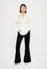 White collared shirt with star patterns in copper and black, paired with black flared pants. Smooth texture, casual fit, and long sleeves.
