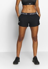 Pantalones cortos deportivos negros con una amplia pretina elástica con el texto "UNDER ARMOUR". Están hechos de un material ligero, tienen bolsillos laterales y un ajuste holgado.