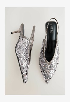 Ezüst flitteres slingback sarokcipők hegyes orral és vékony stiletto sarkakkal. A felsőrész egy texturált felülettel rendelkezik, amely fényvisszaverő díszítésekkel van ellátva.
