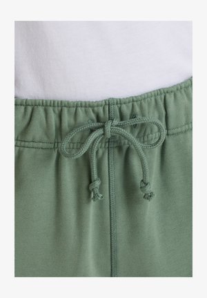 Elastischer Bund mit gebundenem Kordelzug an hellgrünen Jogginghosen vor weißem Hintergrund.