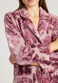 Blazer de tela con estampado floral en tonos morados, con un acabado suave y texturizado. Presenta un cuello de muesca, un bolsillo en el pecho y detalles de botones.