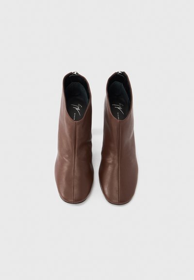 Bottes cheville en cuir marron avec une texture lisse et un design épuré et minimaliste. Dotées d'une fermeture éclair à l'arrière.