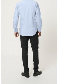 Ljusblå långärmad skjorta med button-down-krage och rundad fåll, kombinerad med svarta slim-fit-byxor och svarta skor, sedd bakifrån.